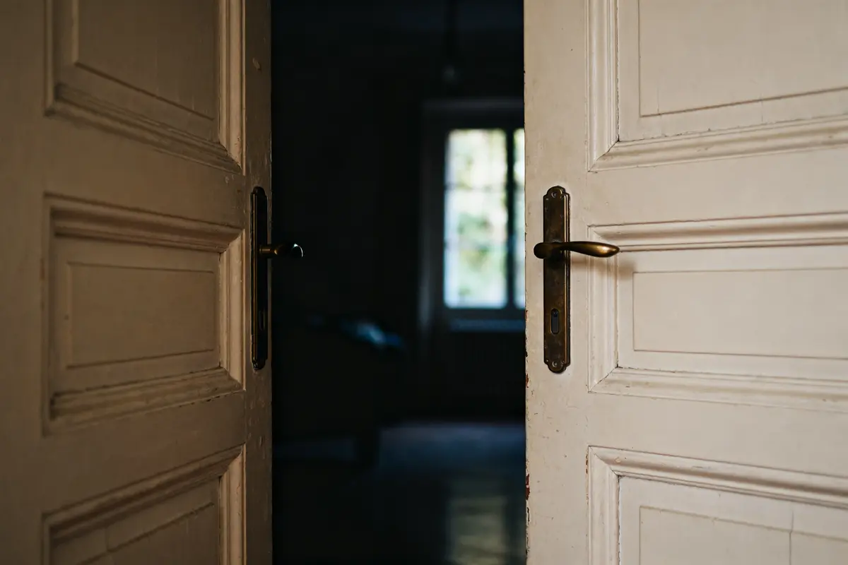 Porte légèrement ouverte poussant vers gauche dévoilant une pièce sombre avec fenêtre floue